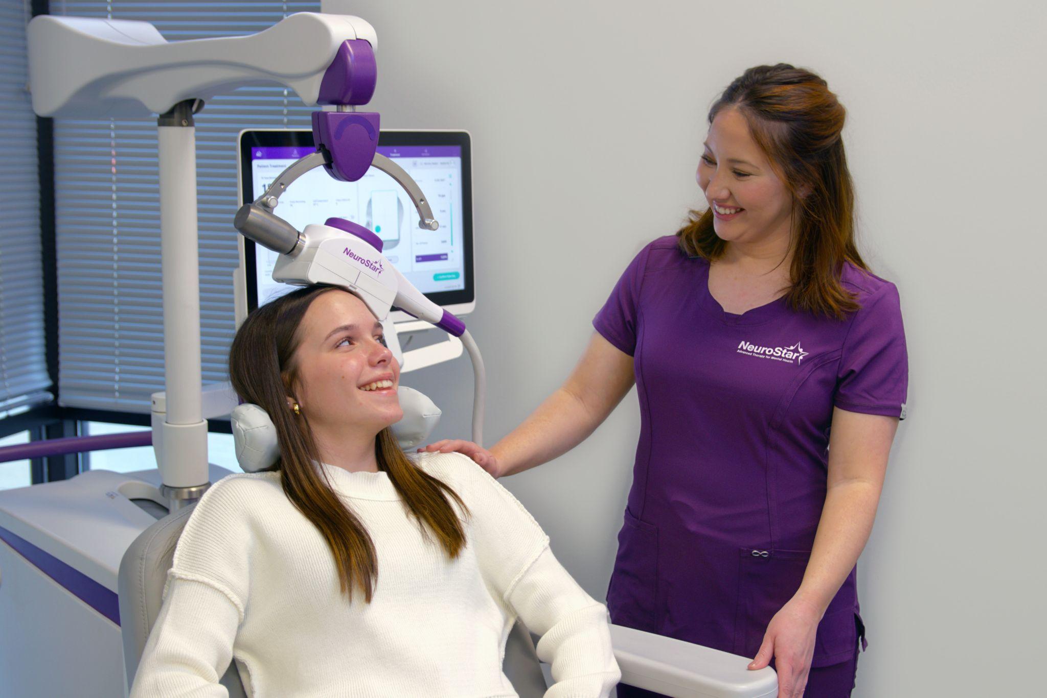 Smiling patient receiving NeuroStar TMS therapy from a clinician in a purple uniform.
