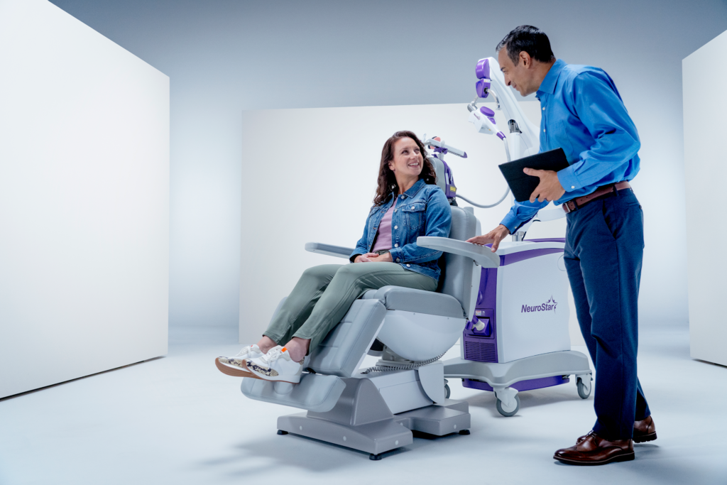 Smiling patient seated in NeuroStar TMS chair talking with doctor before treatment session