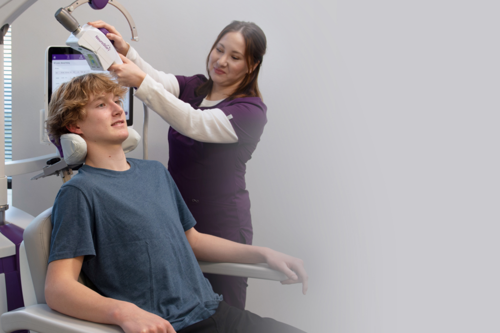 Healthcare provider positioning a NeuroStar TMS coil on a young male patient for OCD treatment.